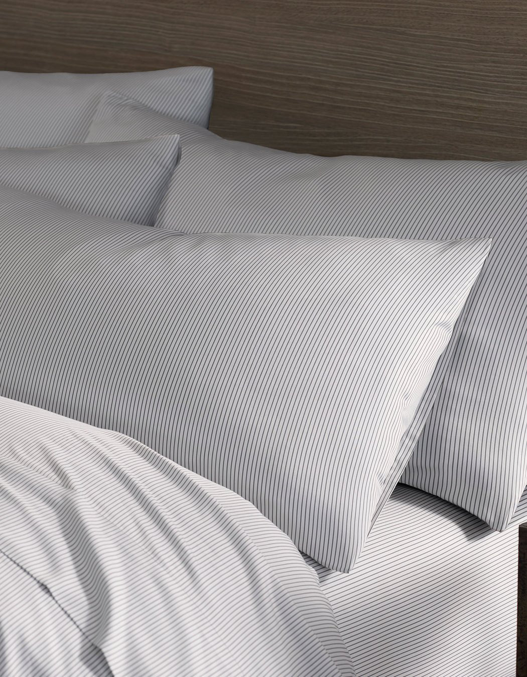 Close-up of a neatly made bed featuring Cozy Earth Bamboo Pillowcases in white and gray pinstripes, set against a dark wood headboard. The arrangement looks clean and inviting.