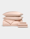 The Bamboo Bedding Ultimate Bundle by Cozy Earth, in light peach, features two stacked pillows, a folded comforter, and neatly folded sheets displayed on a plain light background.|Color:Peony