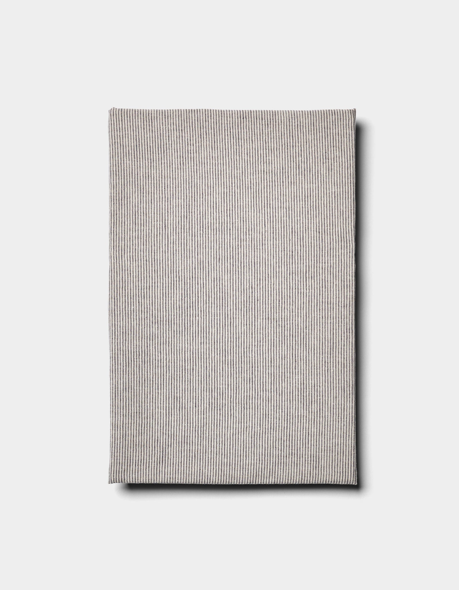 The Baja Double Sided Sham by Cozy Earth is a folded, rectangular, light gray cloth with thin vertical stripes, shown against a plain white background.