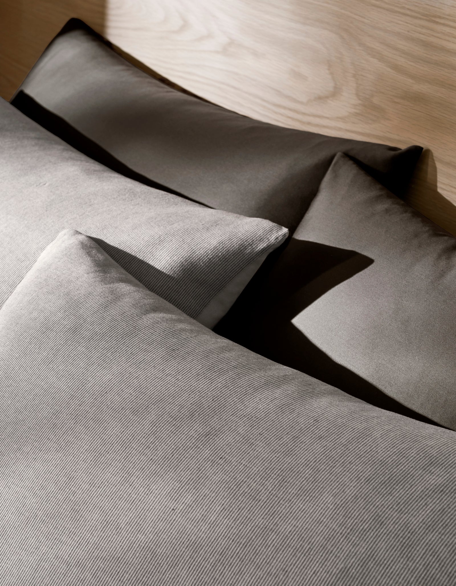 Four neatly arranged Baja Double Sided Shams by Cozy Earth rest on a bed with a light wooden headboard, creating soft shadows and a cozy, minimalistic atmosphere.