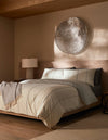 A modern bedroom features a low wooden bed with Cozy Earth's Baja Duvet Cover, beige and gray bedding, a textured throw, a bedside table with a lamp, and large metallic wall art above the bed. Warm neutral tones and soft natural light complete the space.|Color:Coal Stripe/Striped Alabaster