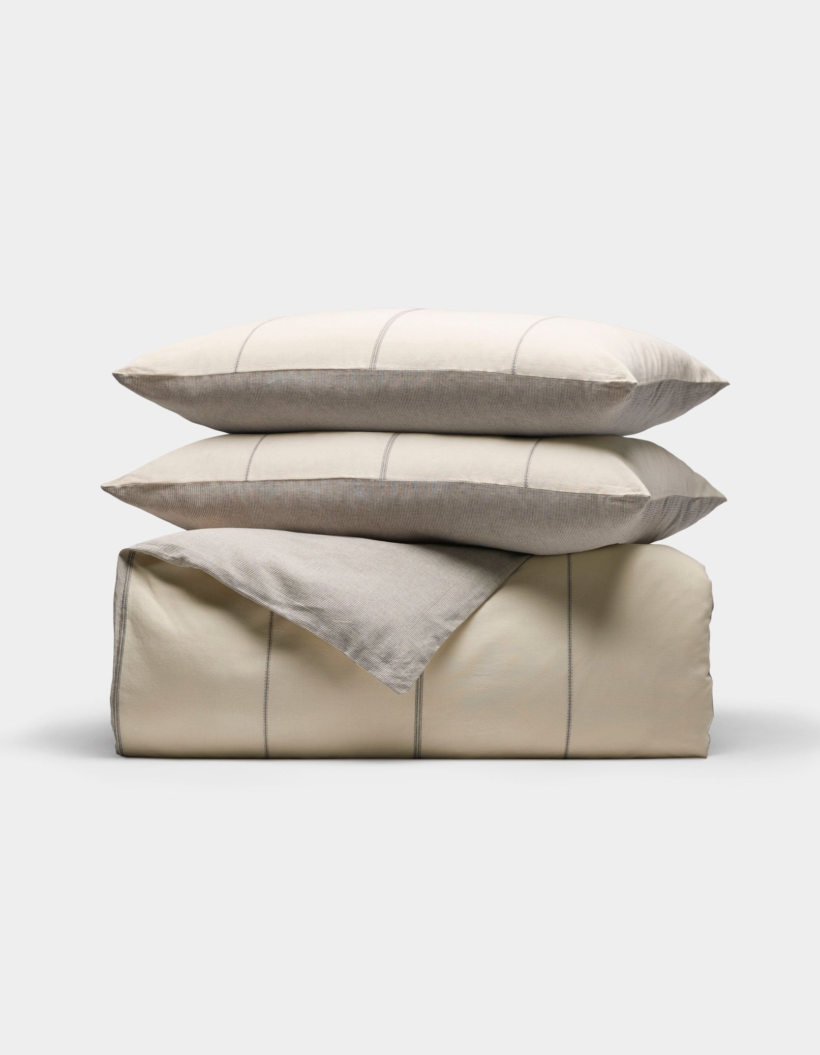 The Baja Duvet Bundle by Cozy Earth features a neatly folded beige comforter with thin light gray stripes, stacked with two matching pillows on top, all set against a plain white background.|Color:Coal Stripe/Striped Alabaster