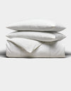 The Cozy Earth Baja Duvet Bundle features two white pillows stacked on a neatly folded white duvet, all set against a plain light grey background.|Color:Laurel Stripe/Striped Bone