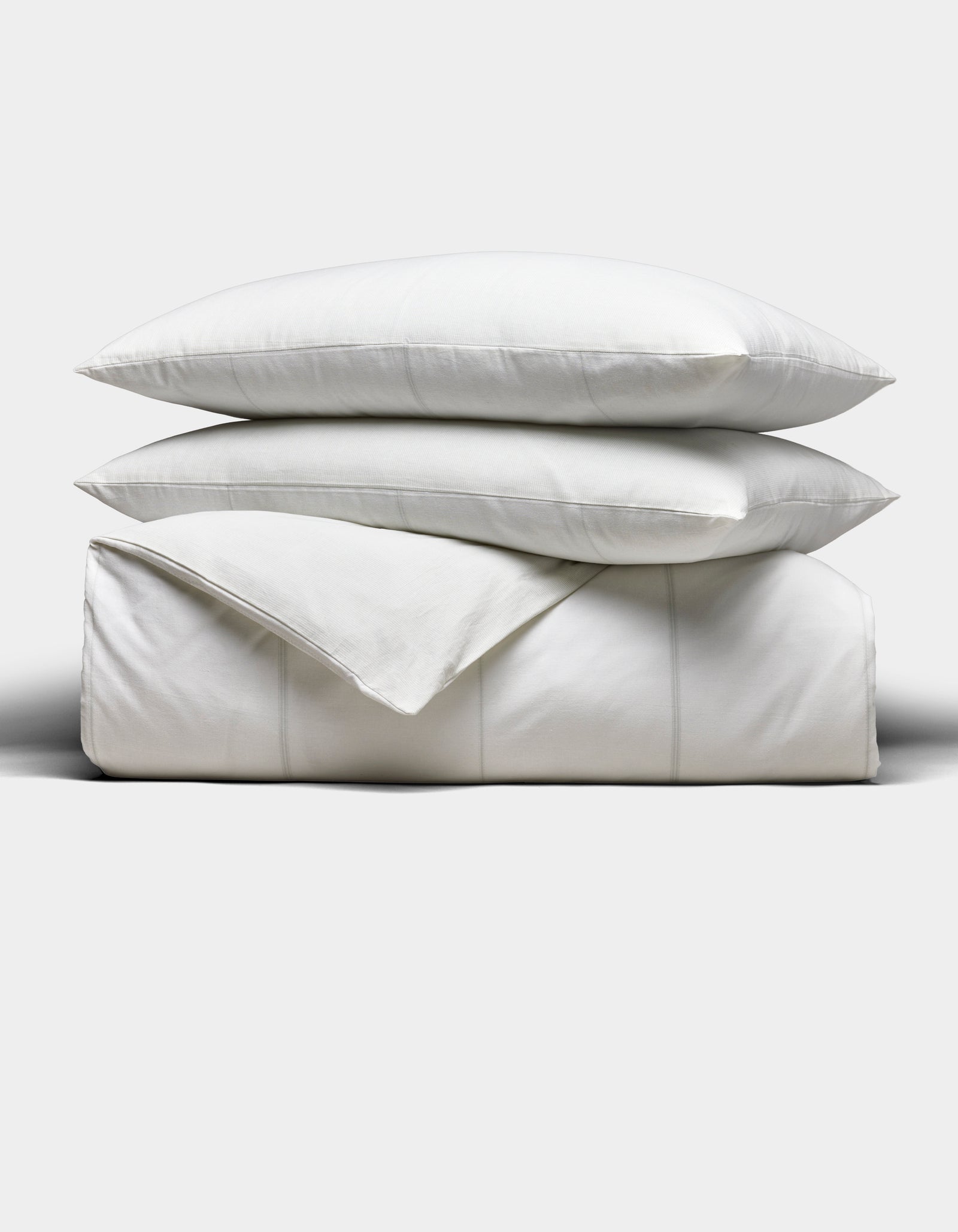 The Cozy Earth Baja Duvet Bundle features two white pillows stacked on a neatly folded white duvet, all set against a plain light grey background.