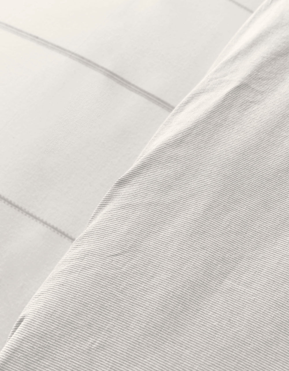 Close-up of Cozy Earth’s Baja Duvet Cover: overlapping white fabrics, one with subtle horizontal stripes and a smooth feel, the other featuring a faint grid pattern. Both offer a soft, clean look.