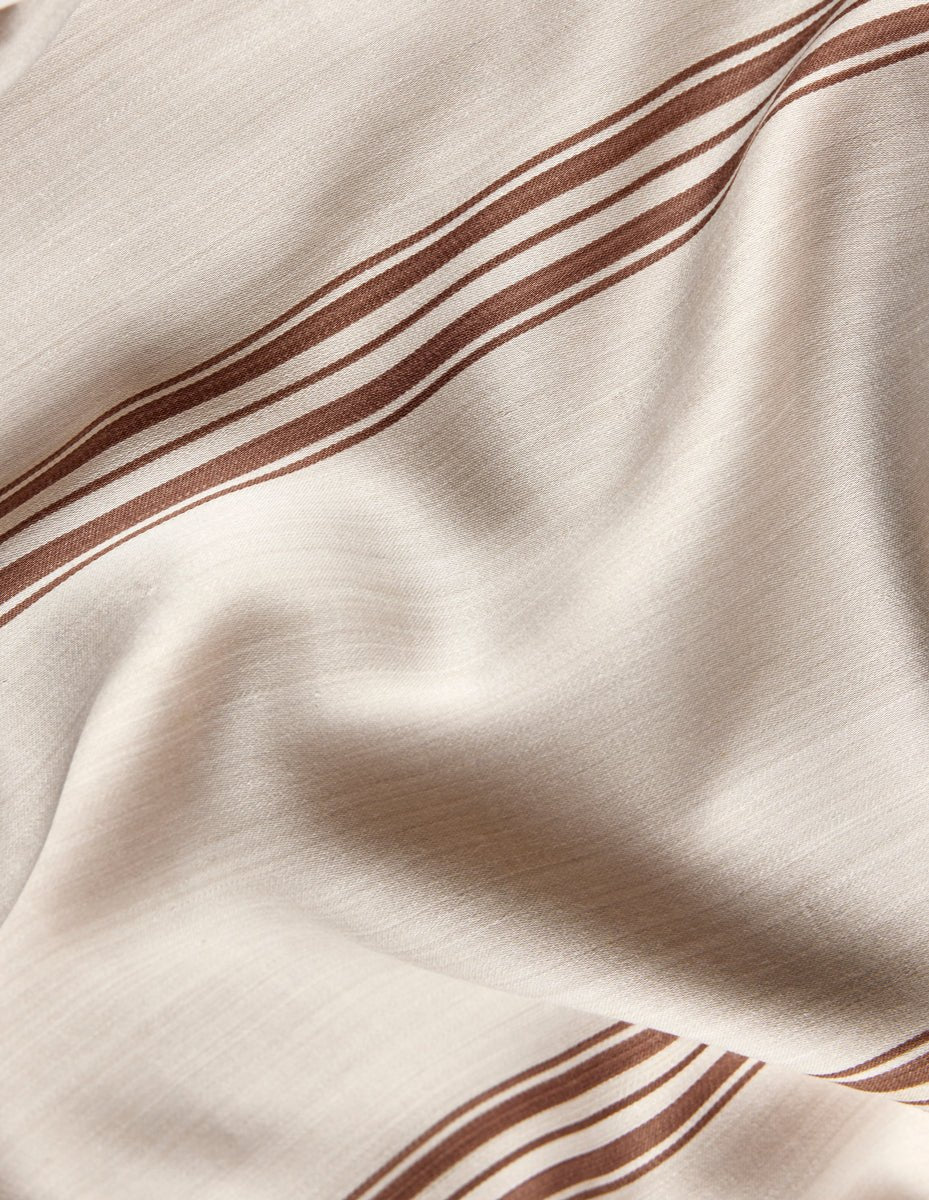 A close-up of Cozy Earth's Bamboo Sheet Set in beige, featuring brown parallel stripes, gentle folds, and a smooth, slightly shiny finish.