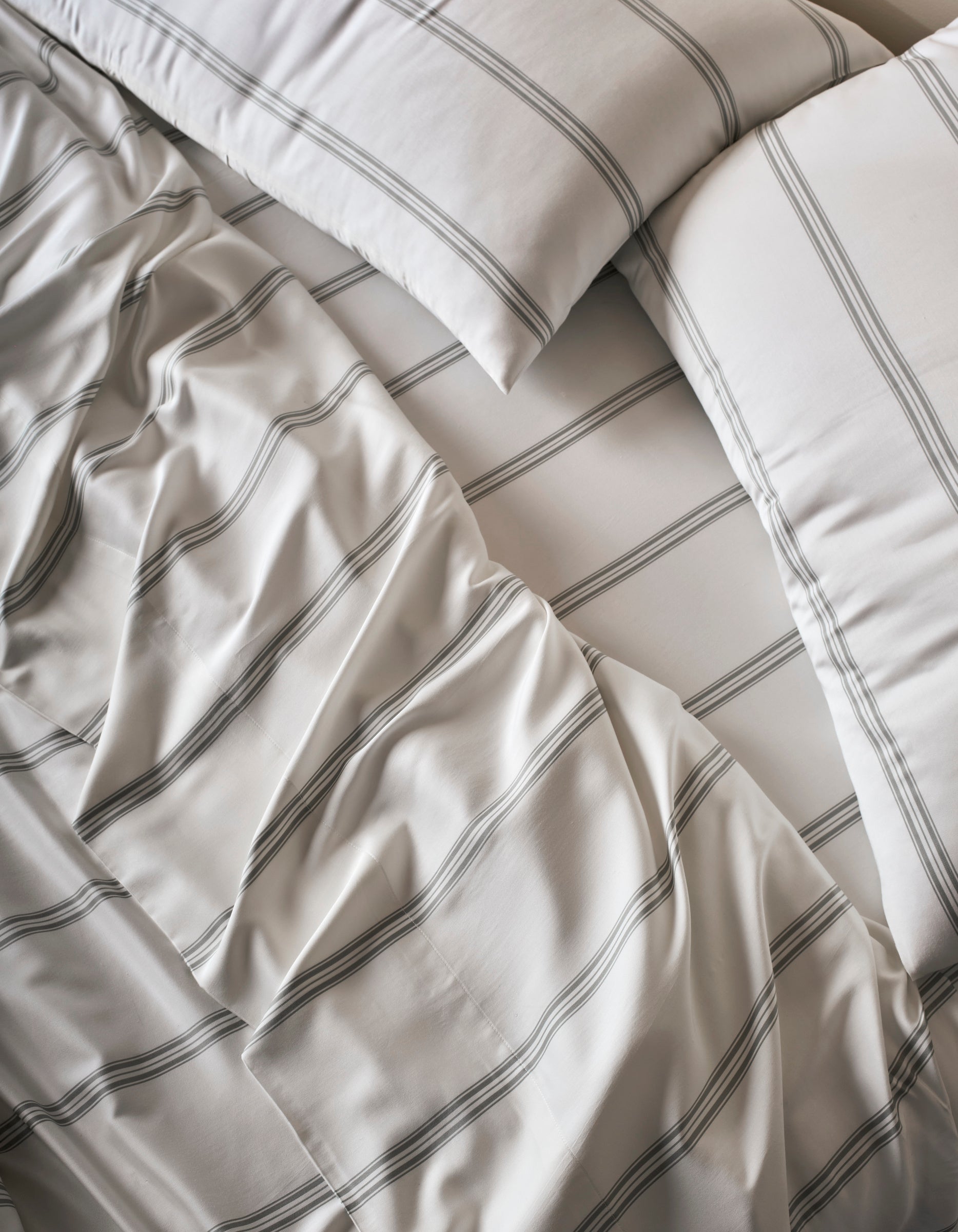 Close-up of a neatly made bed with Cozy Earth's Bamboo Sheet Set—white sheets and pillowcases featuring thin, dark stripes and softly rumpled folds.|Color:Baja Stripe in Laurel