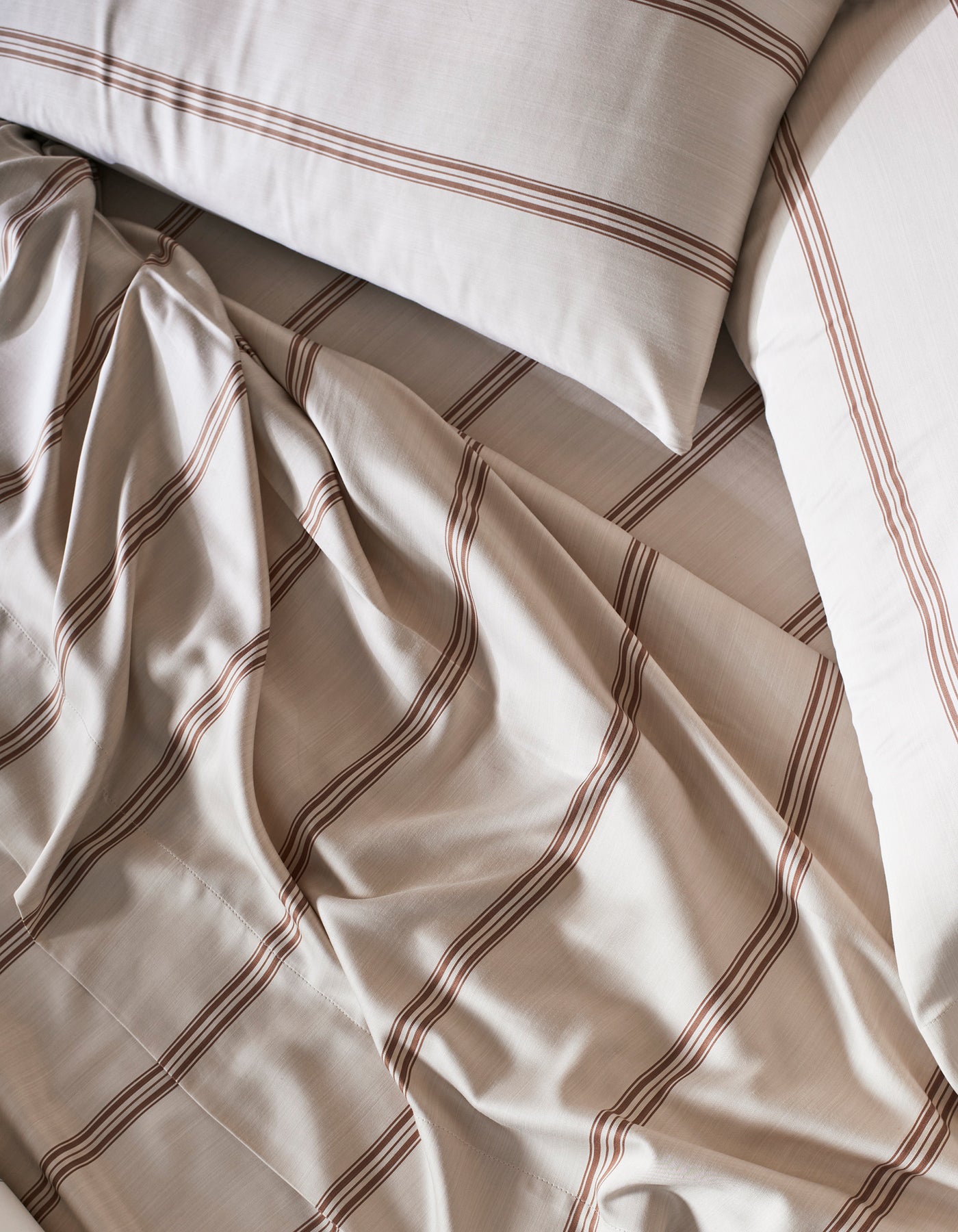 Cozy Earth's Bamboo Pillowcases in beige, featuring brown horizontal stripes, are shown slightly rumpled and overlapping for a casual, inviting vibe.
