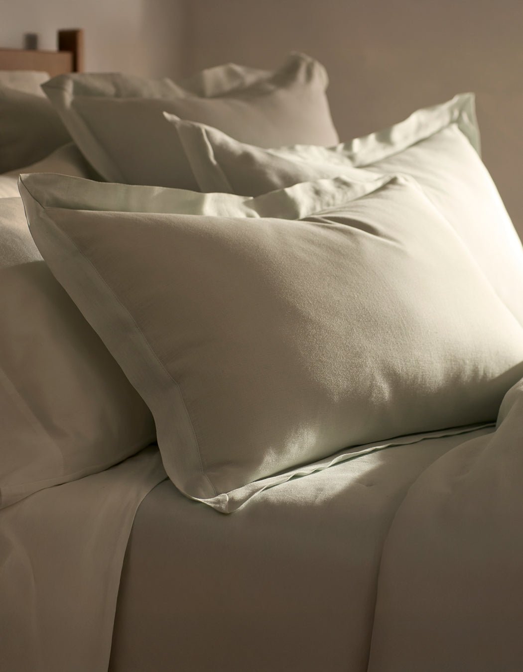 Cozy Earth Linen Shams are neatly arranged on a bed with light beige bedding, beautifully illuminated by soft natural light from the side.