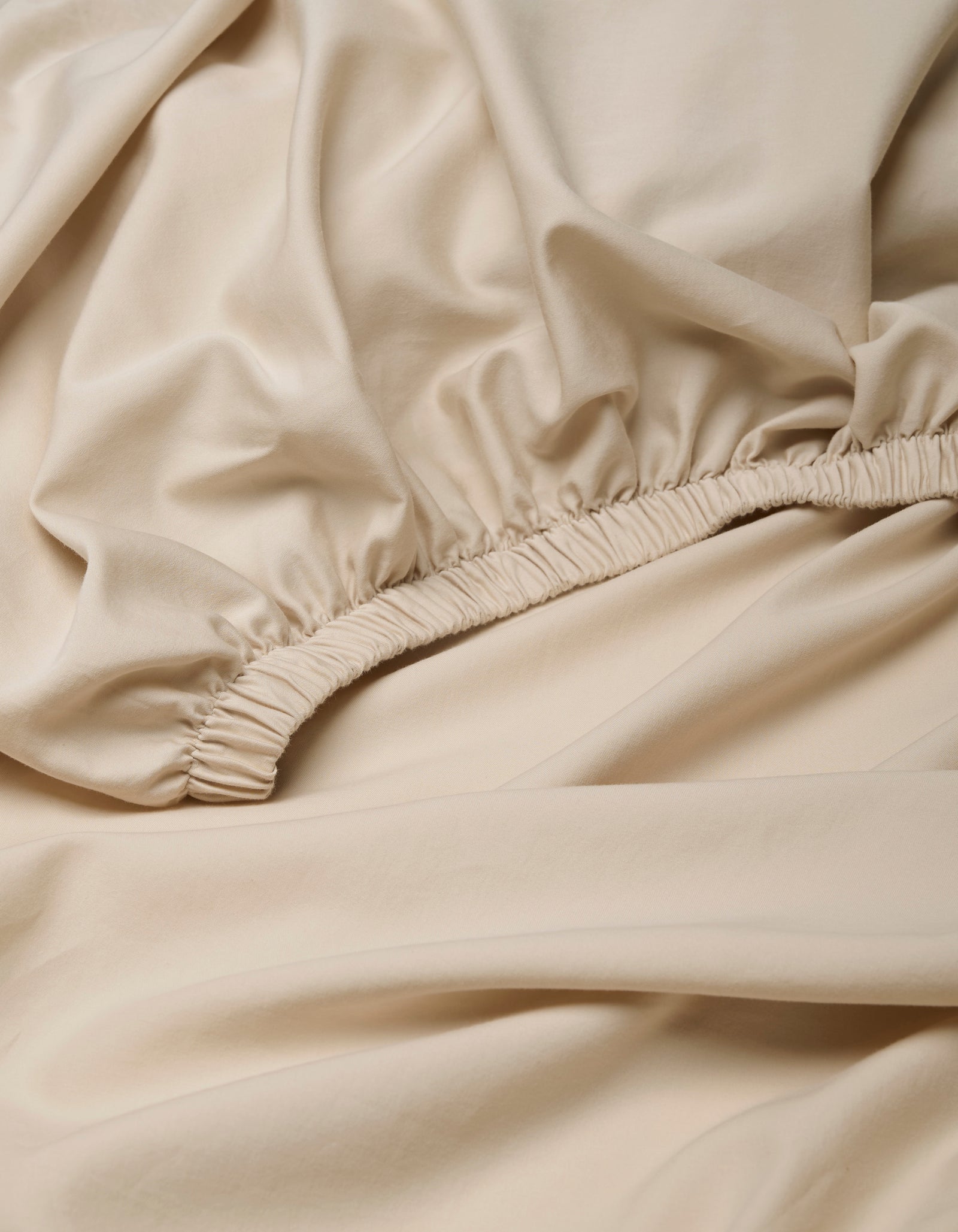 Close-up of beige Soft-Wash Cotton Fitted Sheet by Cozy Earth, featuring smooth fabric with an elastic seam and gathered details.