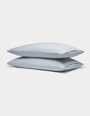 Two Soft-Wash Cotton Pillowcases by Cozy Earth, in light gray, are neatly stacked against a plain white background.|Color:Shore