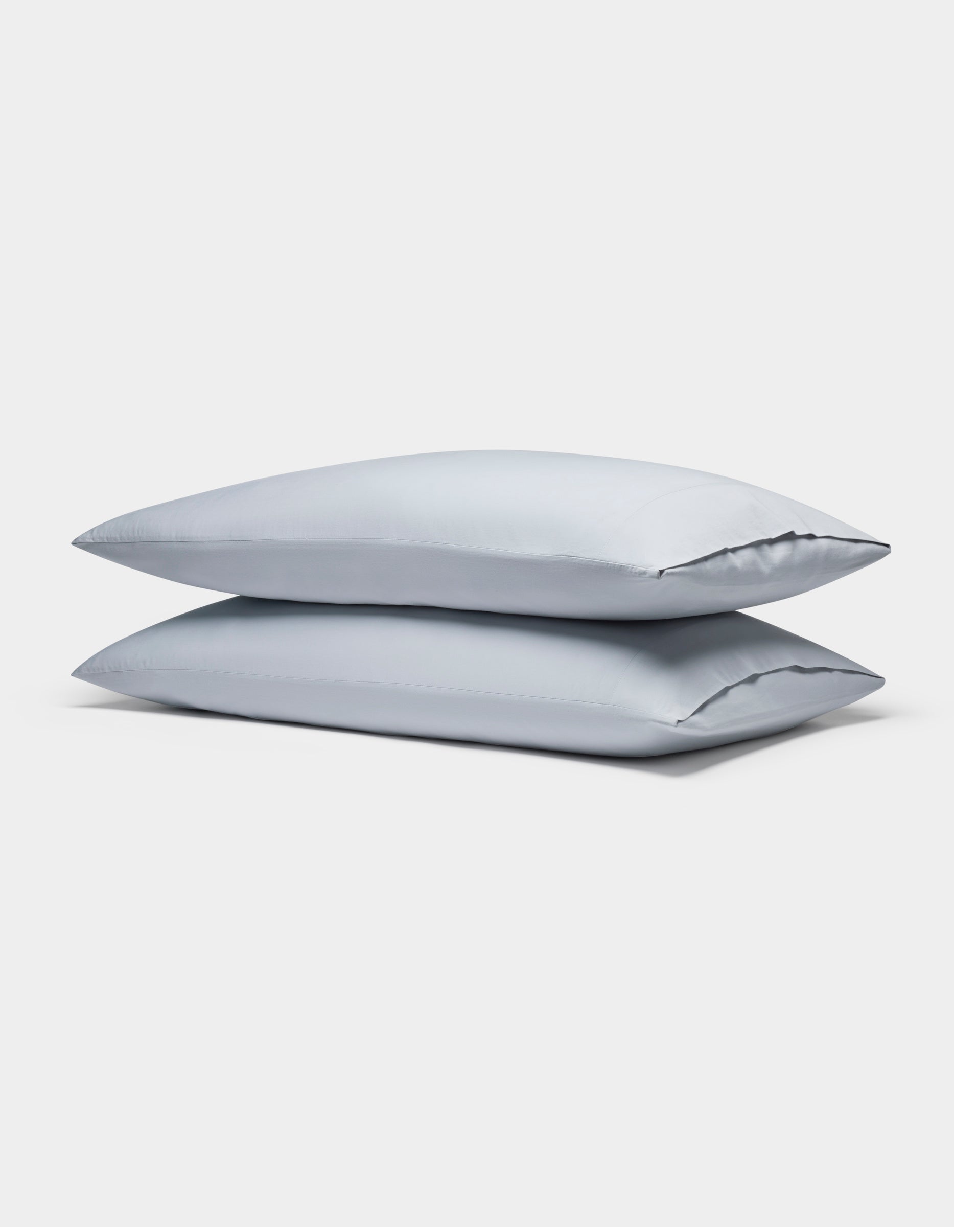 Two Soft-Wash Cotton Pillowcases by Cozy Earth, in light gray, are neatly stacked against a plain white background.|Color:Shore