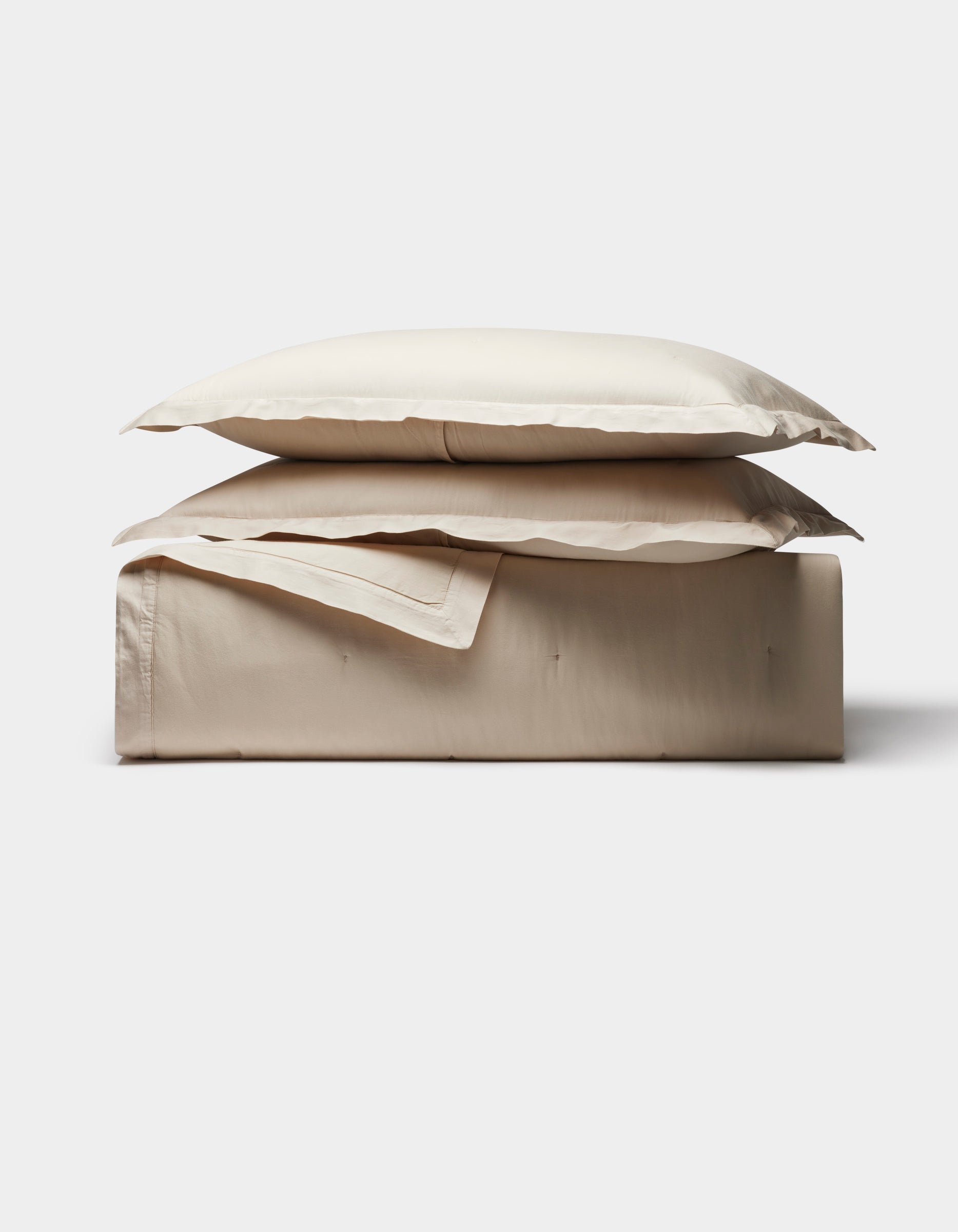 The Cozy Earth Soft-Wash Cotton Quilt Bundle features a neatly folded set of light beige bed sheets and two matching pillowcases, stacked on a plain surface against a white background.|Color:Driftwood