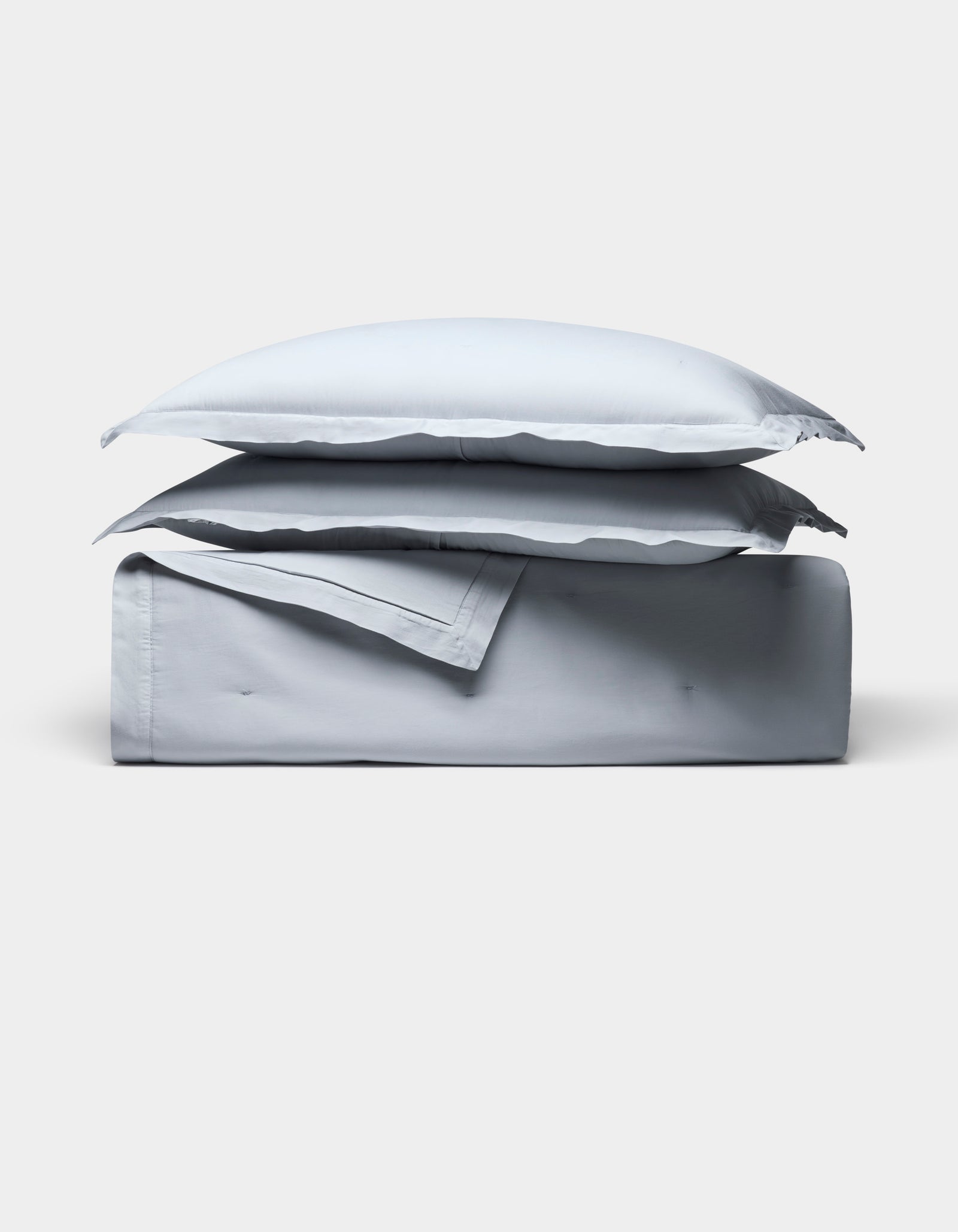 The Cozy Earth Soft-Wash Cotton Quilt Bundle, featuring two pillows and a folded light gray sheet, is neatly stacked and displayed against a plain white background.