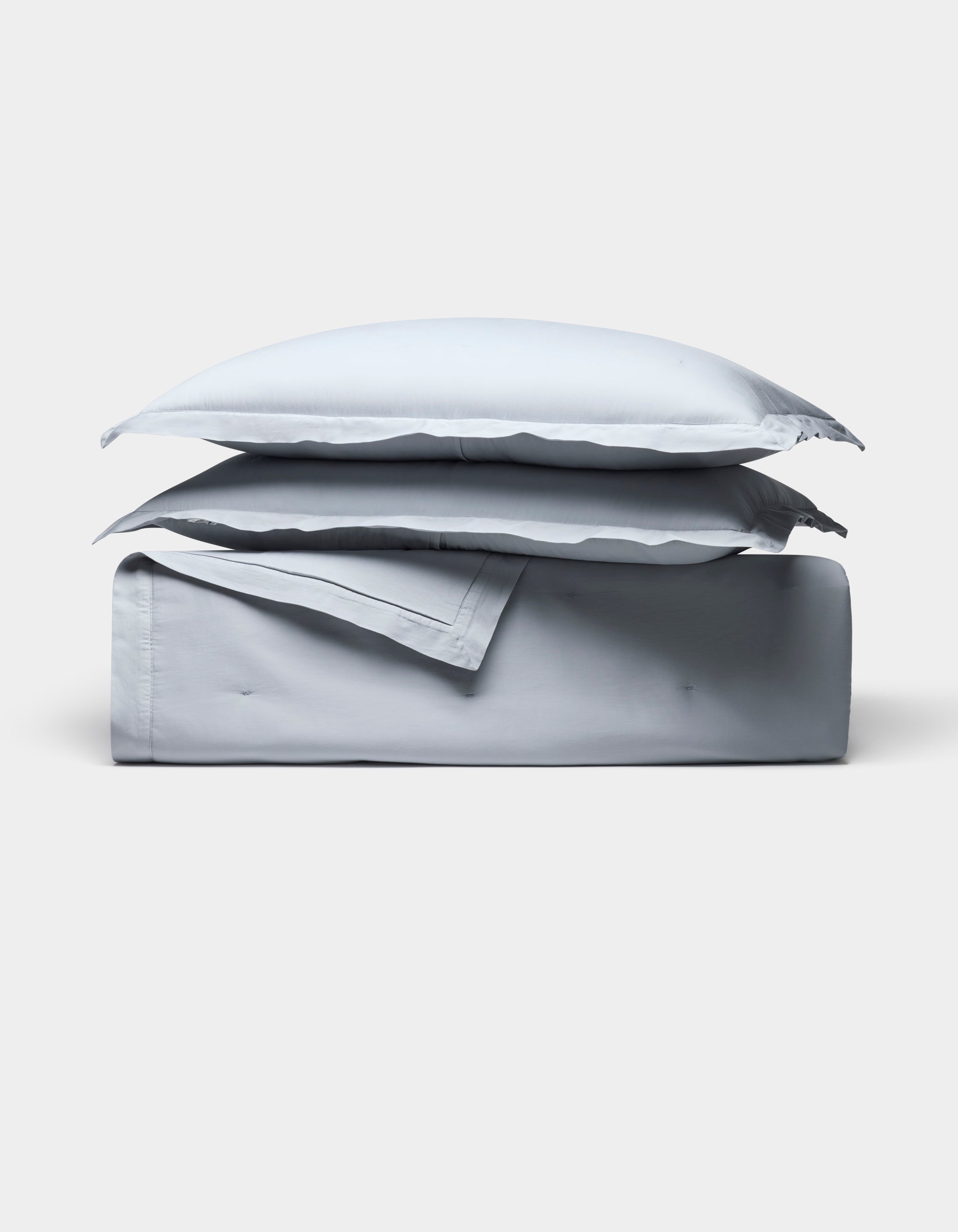 The Cozy Earth Soft-Wash Cotton Quilt Bundle, featuring two pillows and a folded light gray sheet, is neatly stacked and displayed against a plain white background.|Color:Shore