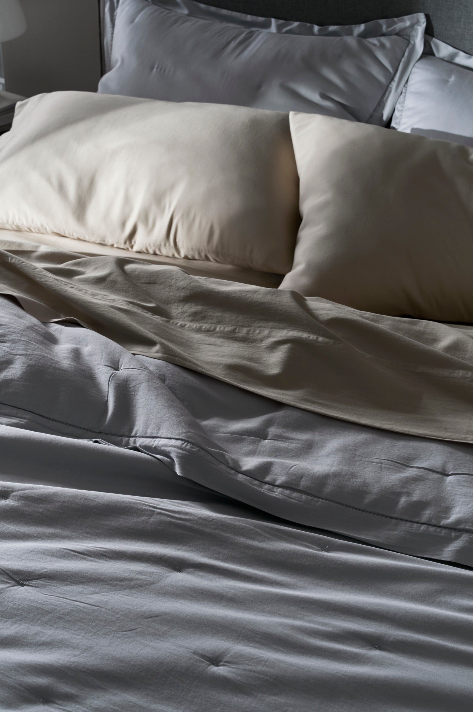 A close-up of an unmade bed features the Cozy Earth Soft-Wash Cotton Quilt with light-colored sheets and two cream pillows, creating a cozy and relaxed vibe with its gently rumpled appearance.