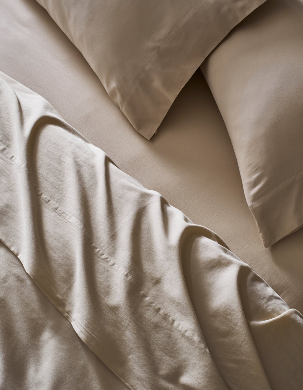 A close-up of a neatly made bed features Cozy Earth's Soft-Wash Cotton Sheet Set in beige. The slightly rumpled sheets and pillowcases enhance the soft, textured look of the smooth fabric.