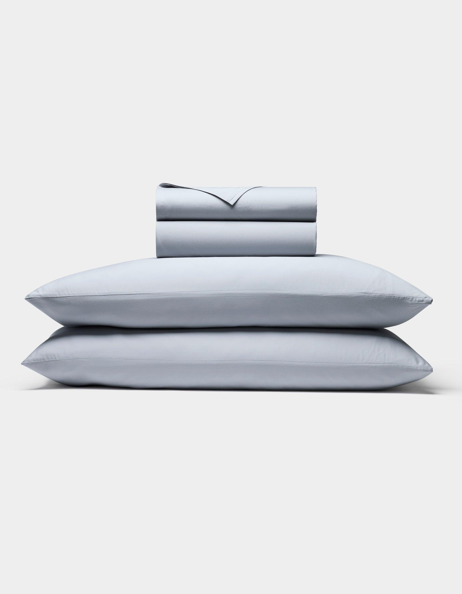 The Cozy Earth Soft-Wash Cotton Sheet Set, in light gray, includes two neatly stacked pillows and a matching folded sheet and pillowcase set, all displayed against a plain white background.|Color:Shore