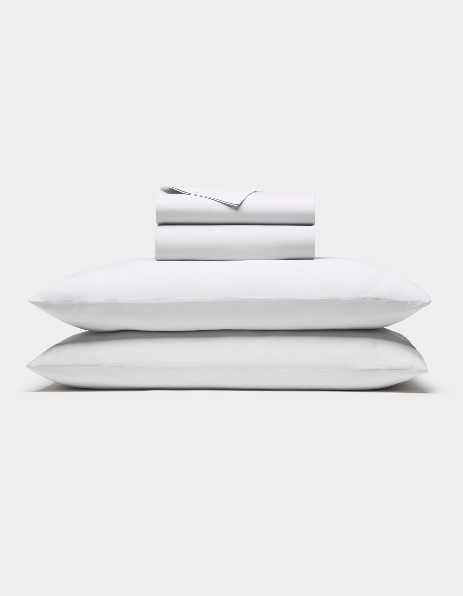The Cozy Earth Soft-Wash Cotton Sheet Set in white, featuring a flat sheet, fitted sheet, and two pillowcases, is shown neatly stacked against a plain white background.