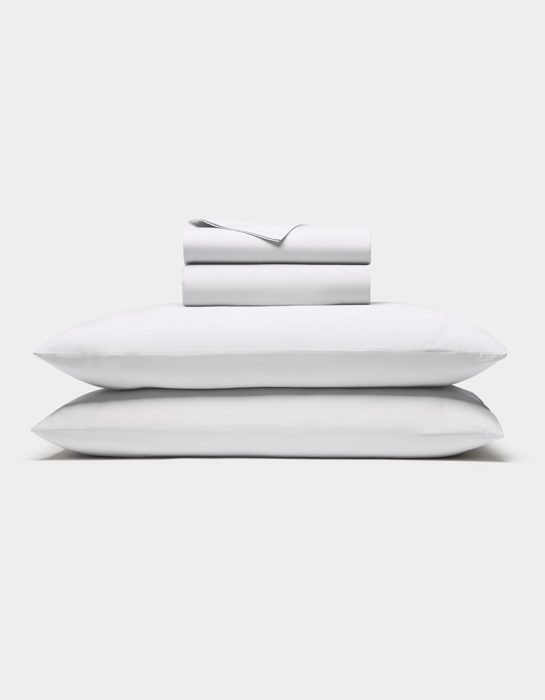 The Cozy Earth Soft-Wash Cotton Sheet Set in white, featuring a flat sheet, fitted sheet, and two pillowcases, is shown neatly stacked against a plain white background.|Color:White