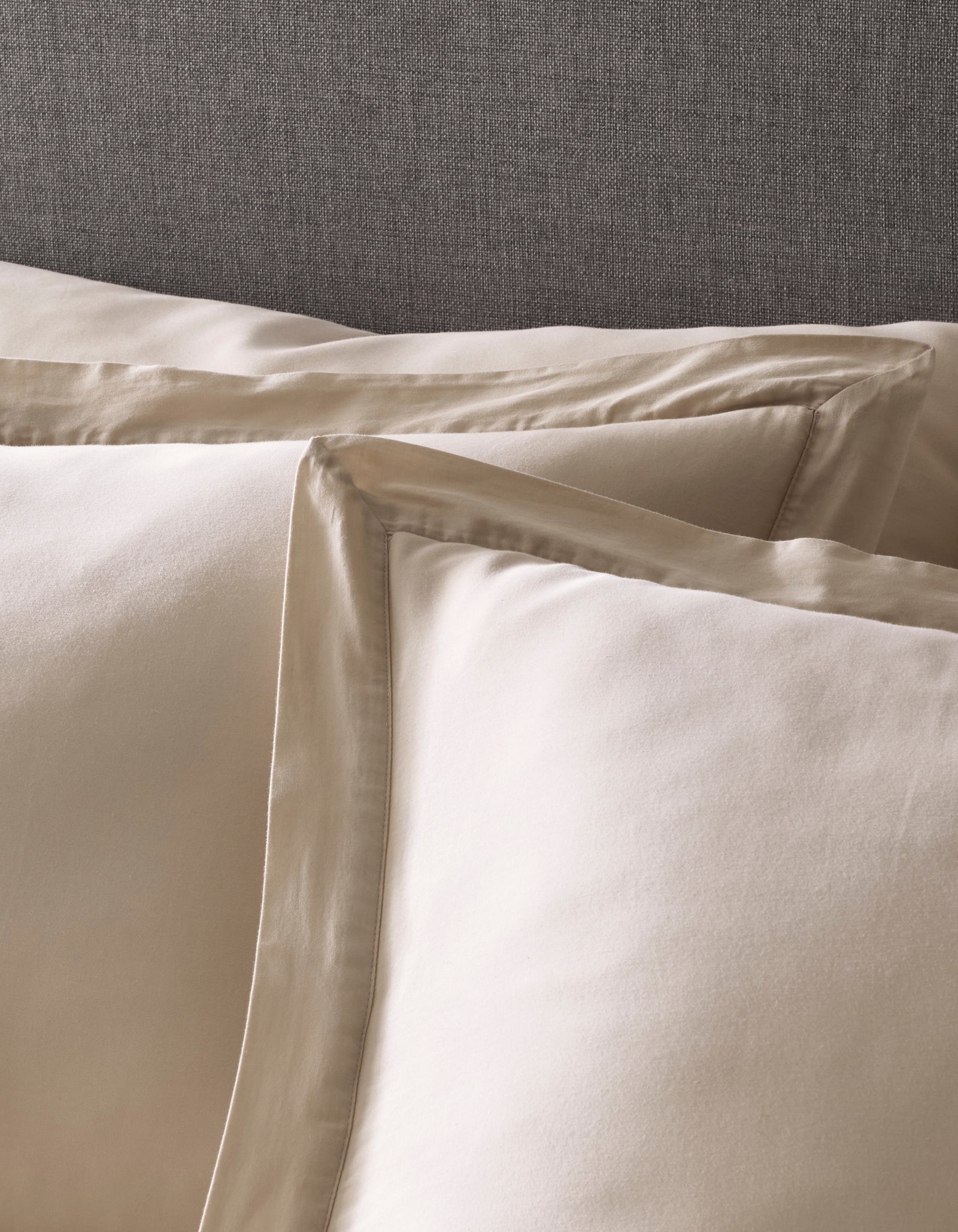 Close-up of two Cozy Earth Soft-Wash Cotton Shams with satin trim, displayed in front of a gray upholstered headboard.