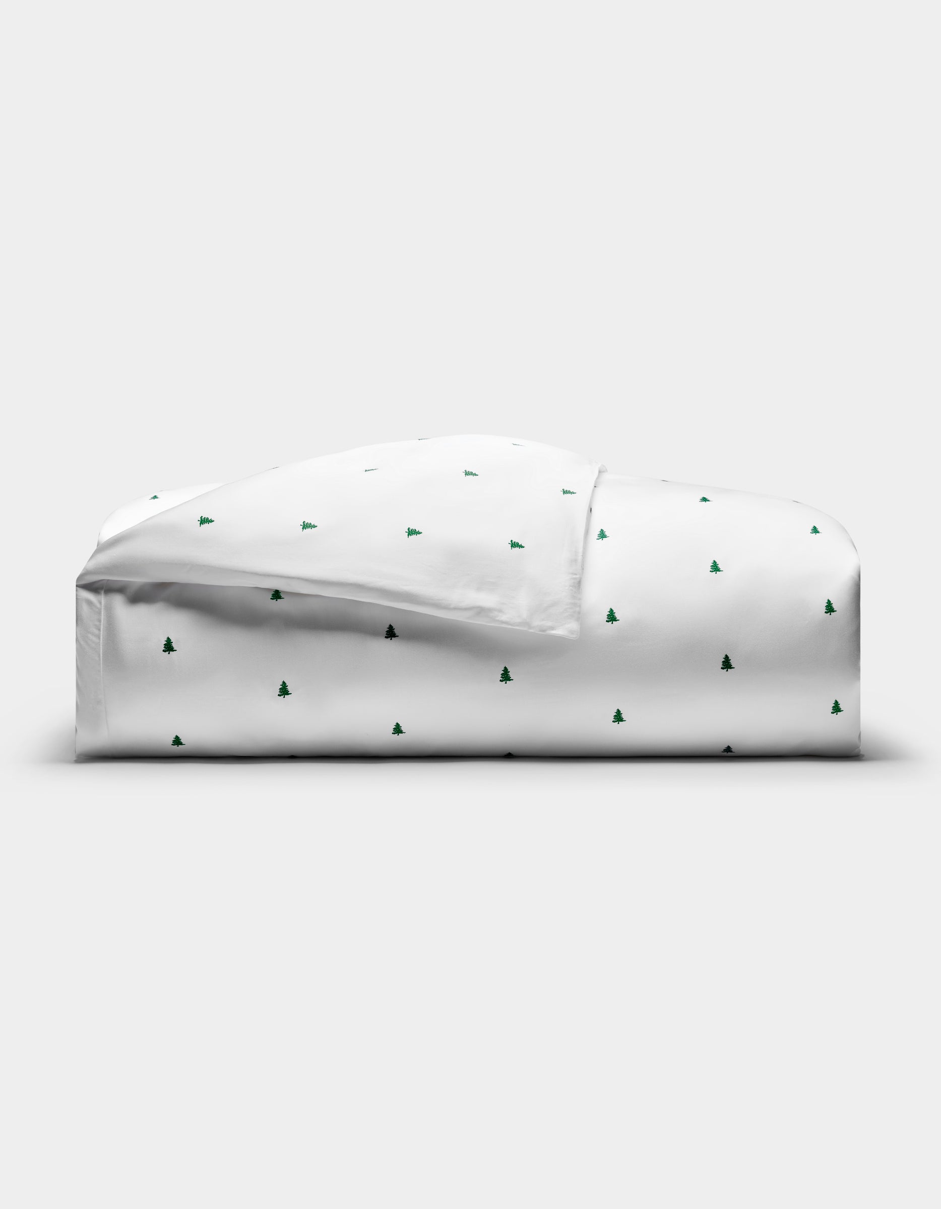 The Cozy Earth Bamboo Duvet Cover, featuring a minimal pattern of small green Christmas trees, is neatly folded on a plain white background.|Color:Jade Tree Snow