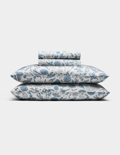 The Cozy Earth Bamboo Sheet Set, featuring pillowcases and sheets with a blue floral pattern on a white background, is neatly folded and displayed against a plain white backdrop.|Color:Winter Toile Pacific