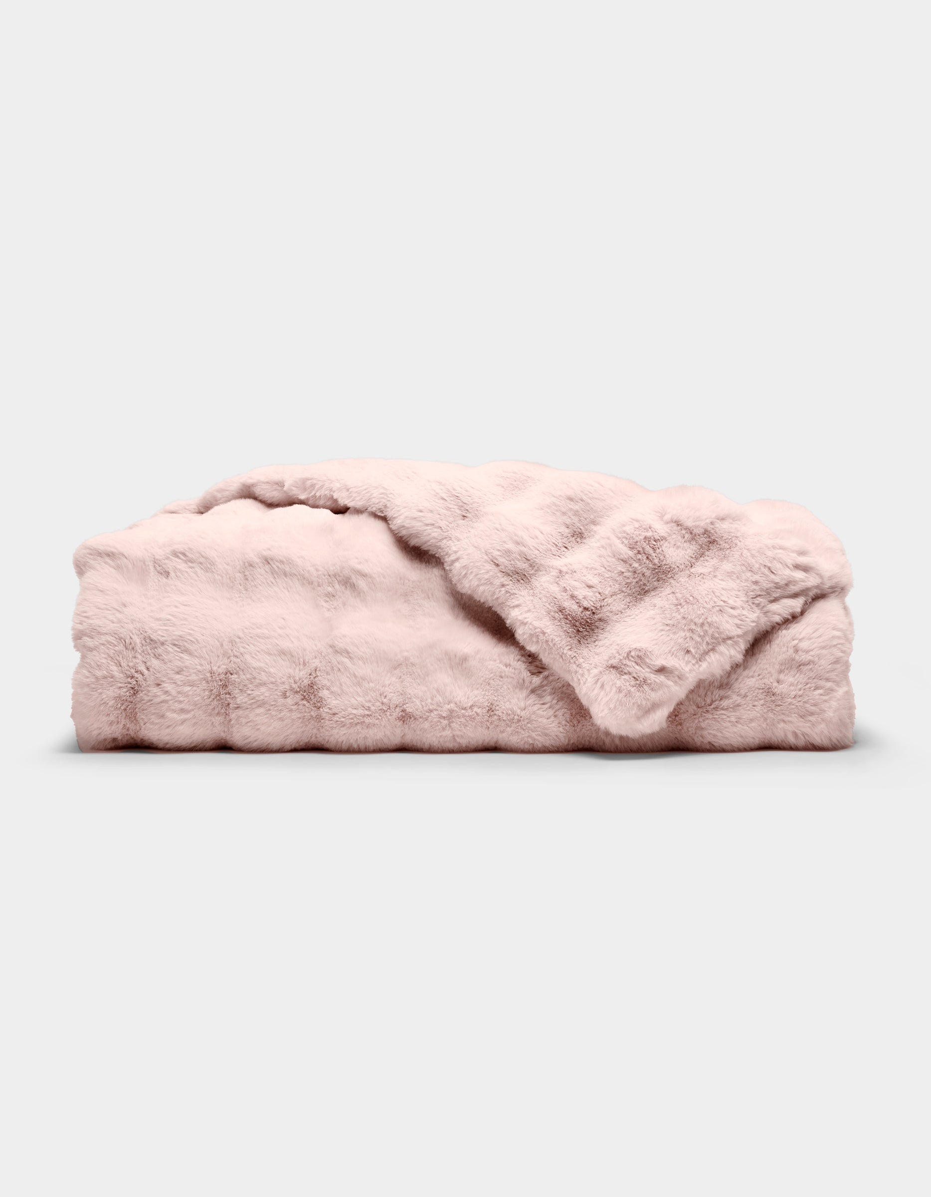 The Bubble Cuddle Blanket by Cozy Earth, in pale pink faux fur, is shown folded on a light gray background with one corner draped to reveal its soft texture.|Color:Blossom