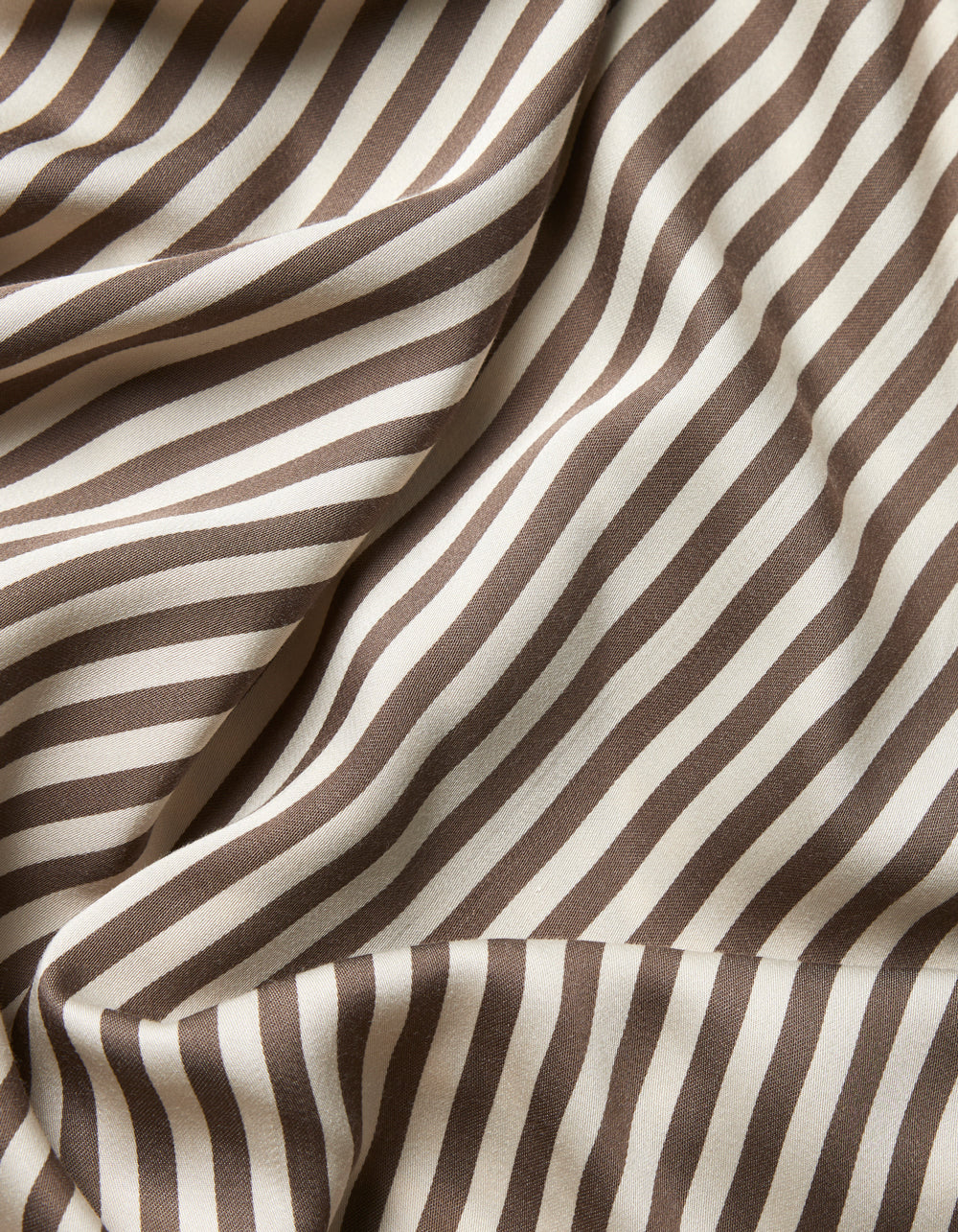 Close-up of Cozy Earth’s Bamboo Sheet Set fabric, featuring diagonal brown and white stripes with soft folds and a smooth texture that creates a dynamic, wavy effect across the material.|Color:Classic Stripe in Ebony