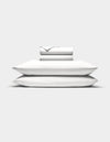 Two white Cozy Earth Bamboo Jersey Sheet Set sheets are neatly folded atop two stacked pillows, all set against a plain white background.|Color:White