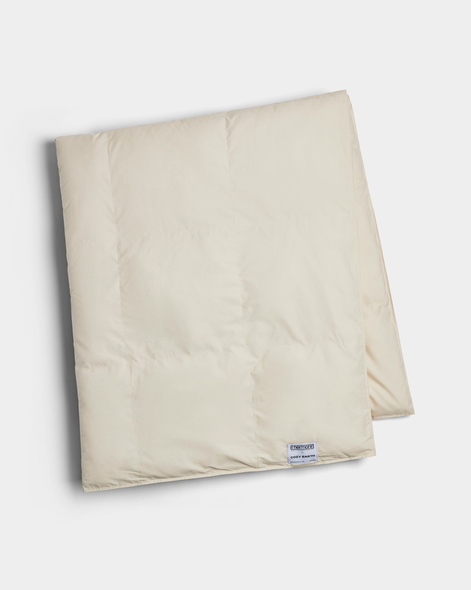 The Cozy Earth Down Alternative Throw is a folded, cream-colored quilt with a small rectangular label near the edge, displayed on a white background.