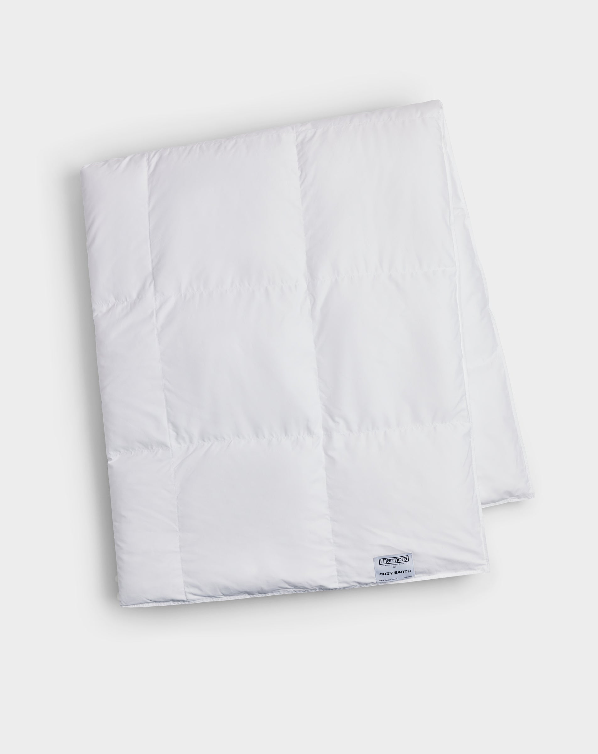 The Cozy Earth Down Alternative Throw, in white with stitched squares and a small corner label, is neatly folded and displayed on a plain light background.|Color:White