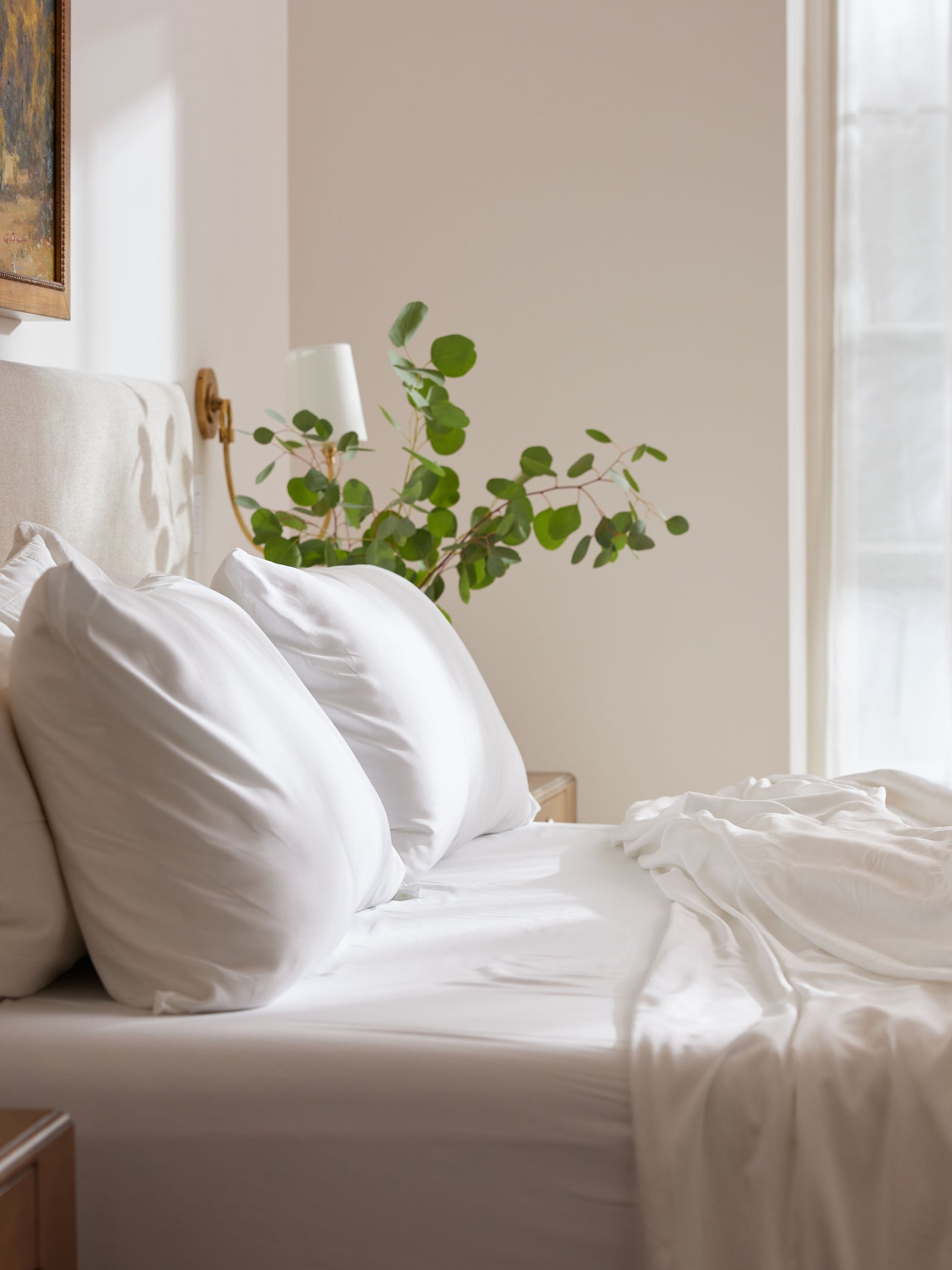 White bedding on bed with plant behind it 