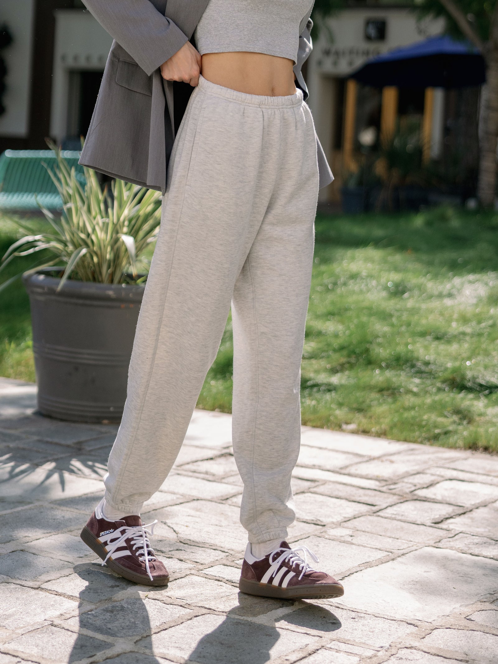 Heather Grey CityScape Joggers. The Joggers are being worn by a female model. The photo is taken from the waist down with the models hand by the pocket of the joggers. The back ground is the back yard of a home. 