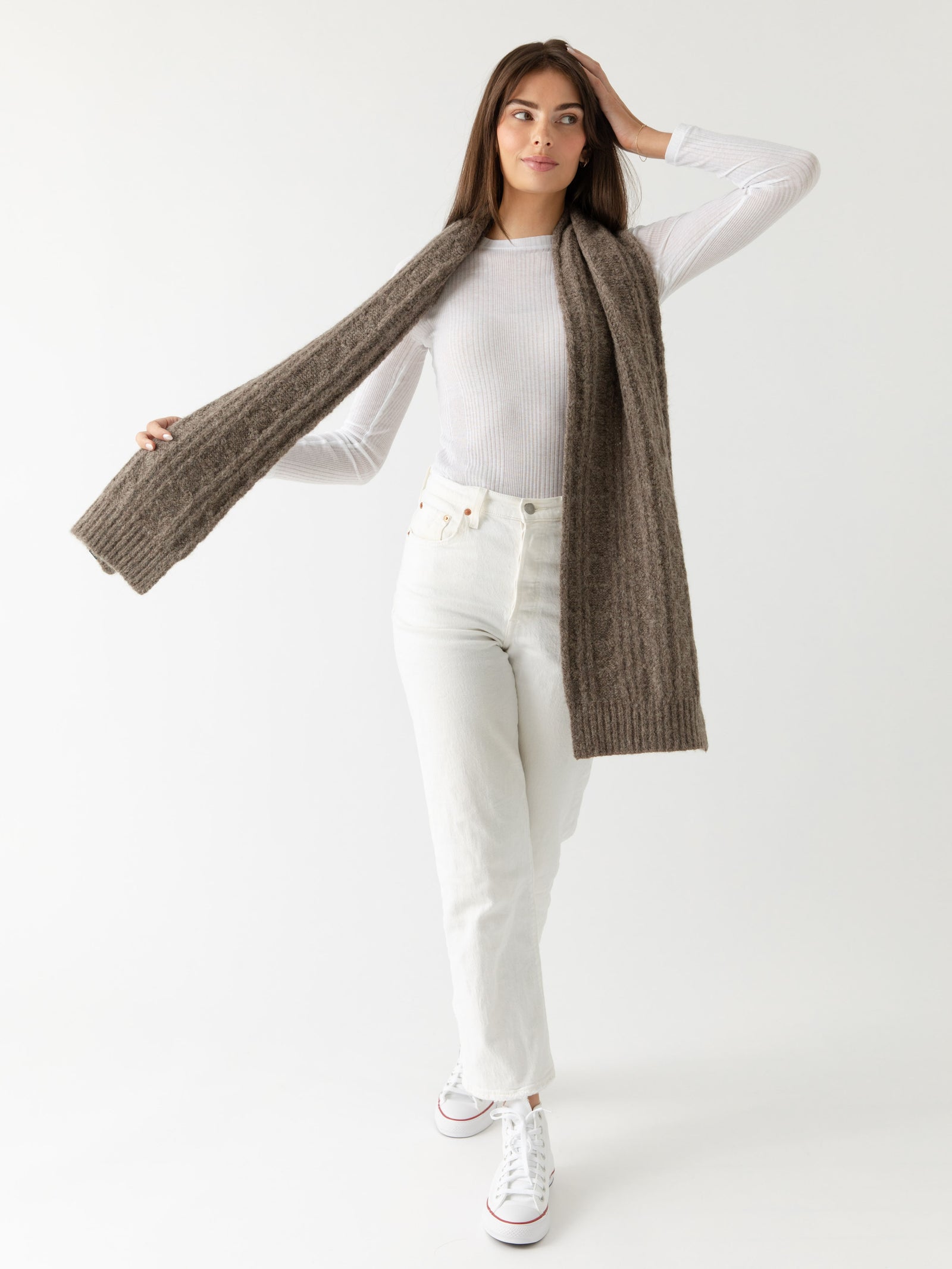 Woman wearing a brown knit cardigan, Cozy Earth Cable Knit Scarf stands in front of a white background