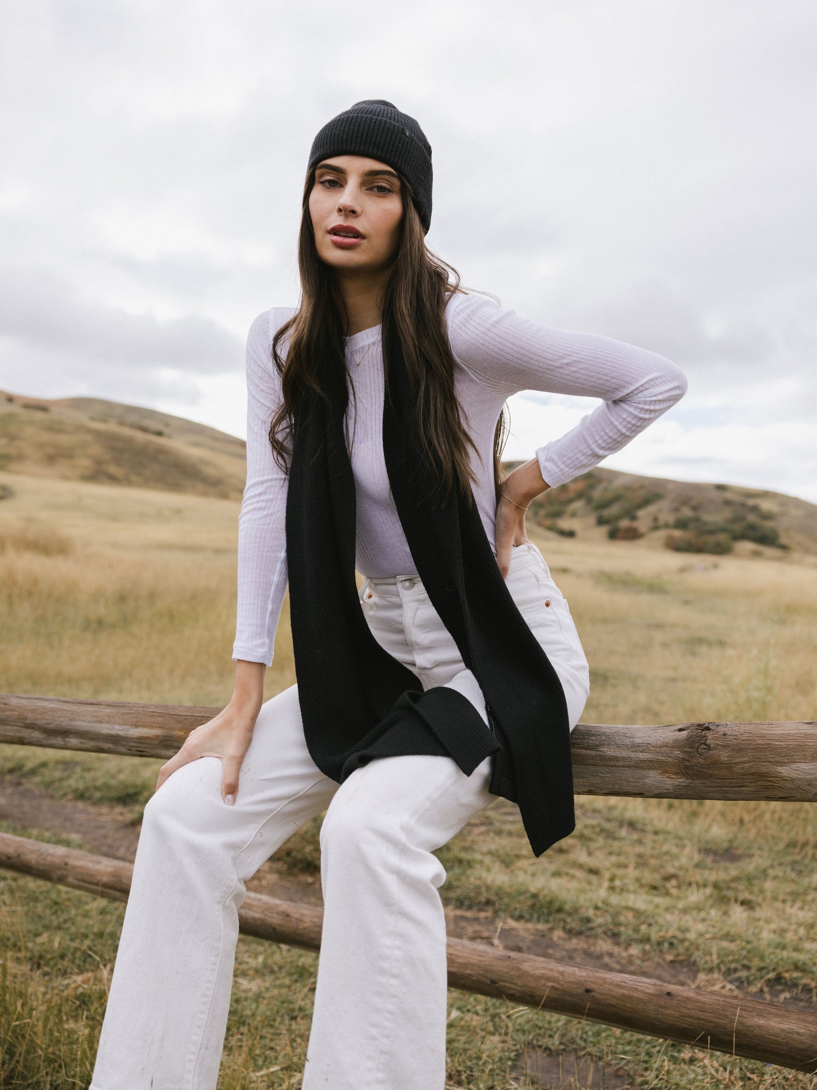 Person wearing a black scarf, white sweater, and light-colored pants in a field