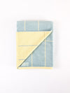 The Cozy Earth Windowpane Resort Towel, folded to reveal its blue side with yellow lines atop and the yellow side with blue lines underneath, is neatly arranged on a plain white background. |Color:Blue Lagoon