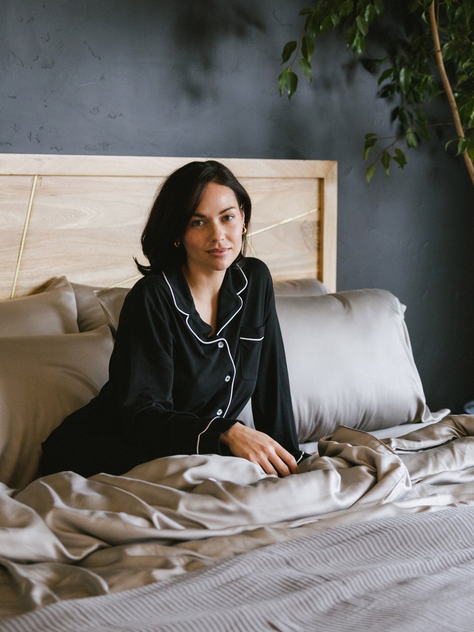 Woman in black pajamas sitting in bed with dove grey sheets 