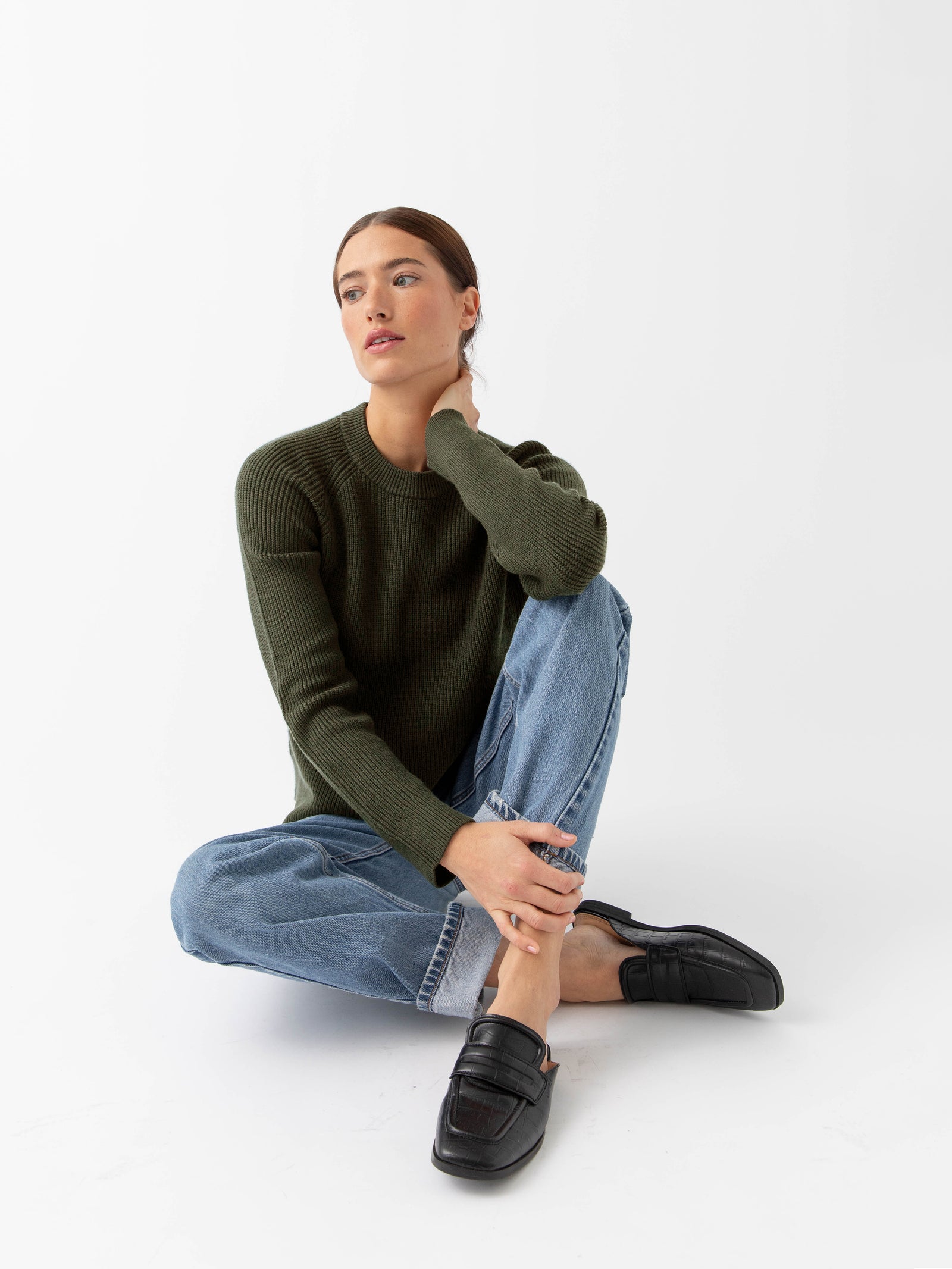Woman sitting wearing juniper classic crewneck and jeans with white background