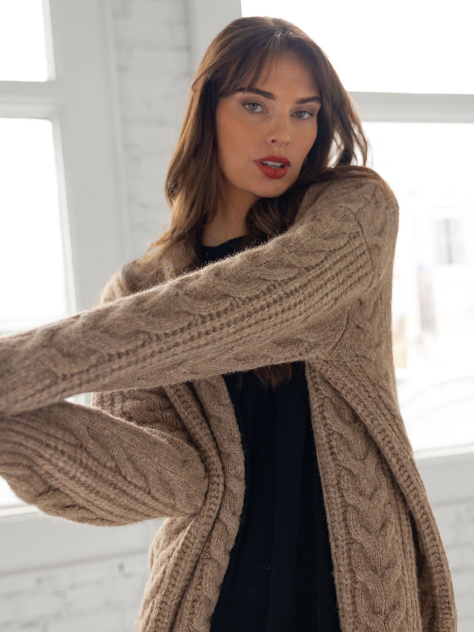 Close up of woman in mushroom cardigan over black dress in front of windows