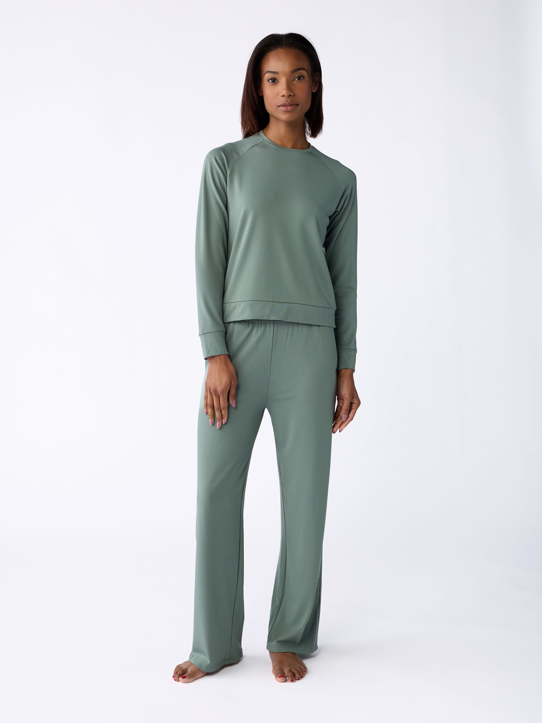 A person stands barefoot against a white background, wearing a sage green long-sleeve top and matching Women's Ultra-Soft Bamboo Wide Leg Pull On Pants from Cozy Earth. |Color:Oakmoss