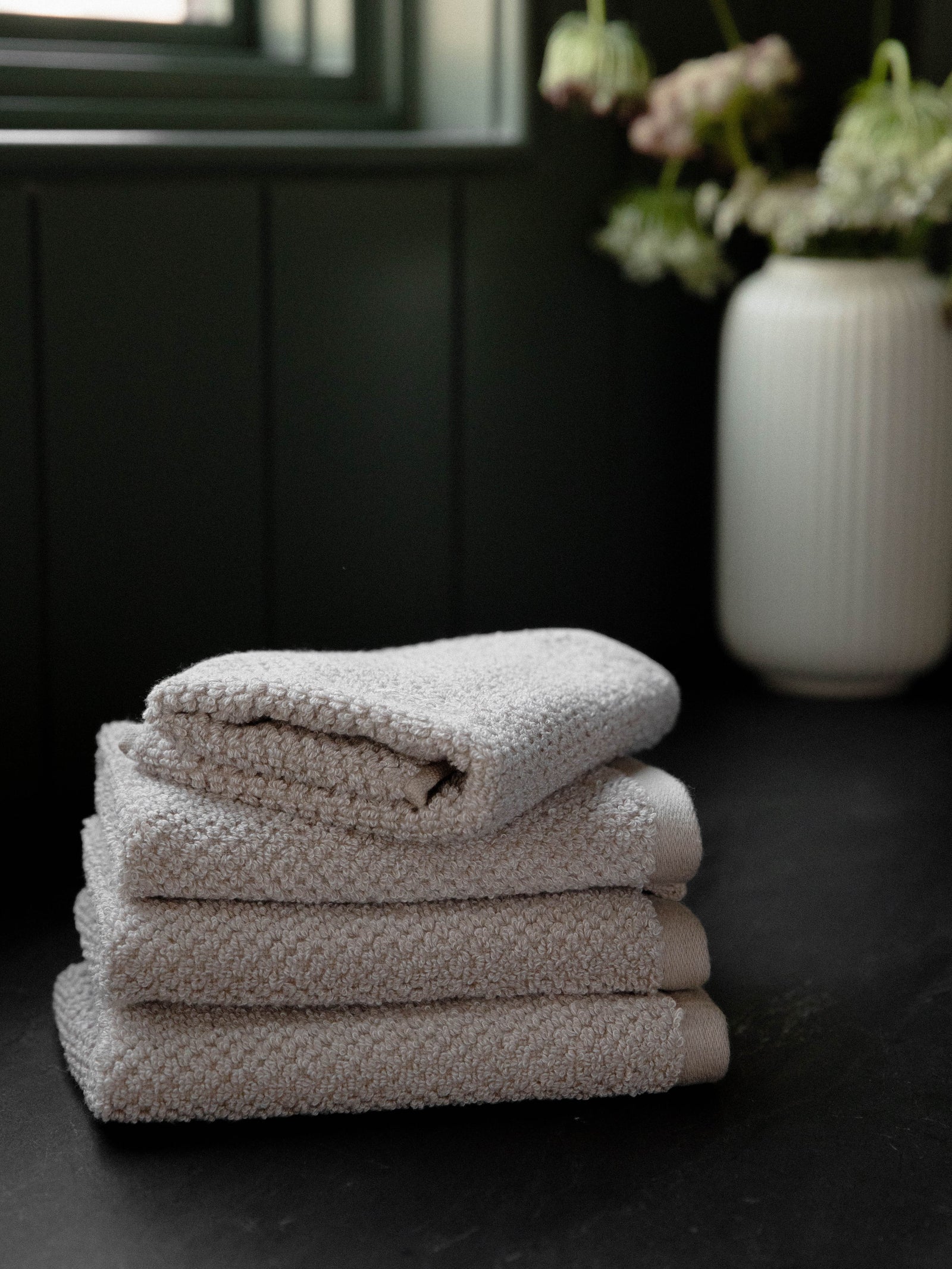 Nantucket Wash Cloths in the color Heathered Sand. Photo of Nantucket Wash Cloths taken with the Wash Cloths resting on a countertop in a bathroom. 