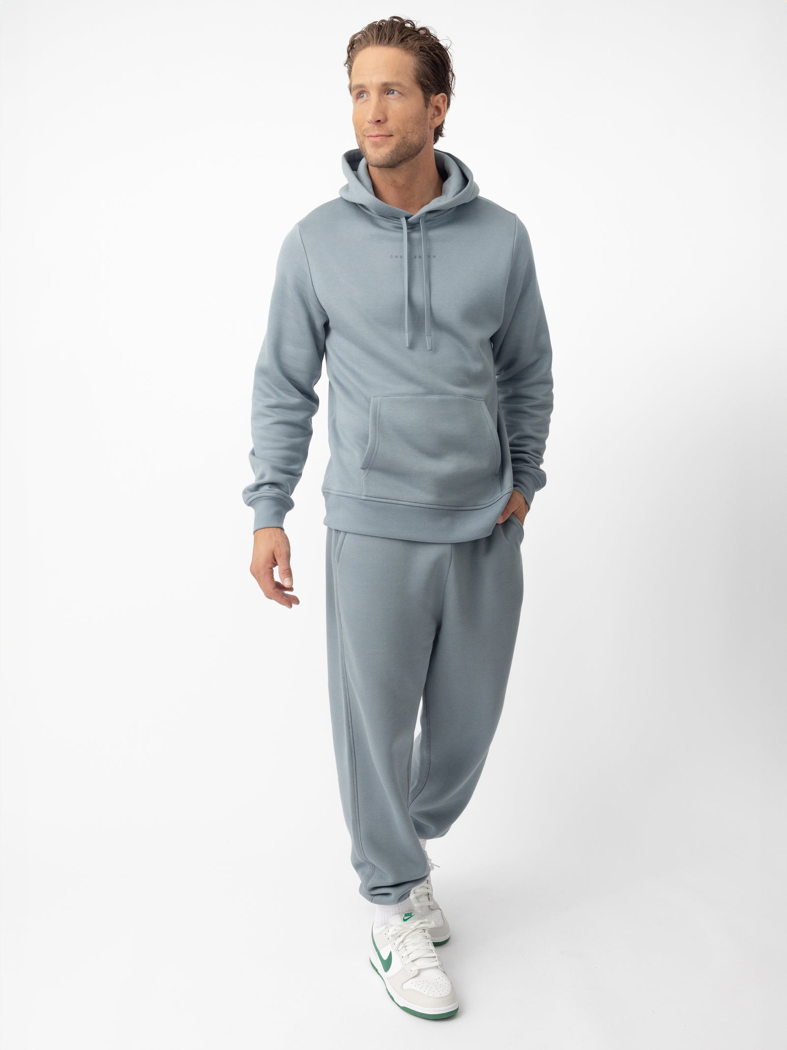 Man wearing smokey blue cityscape hoodie and sweats with white background 