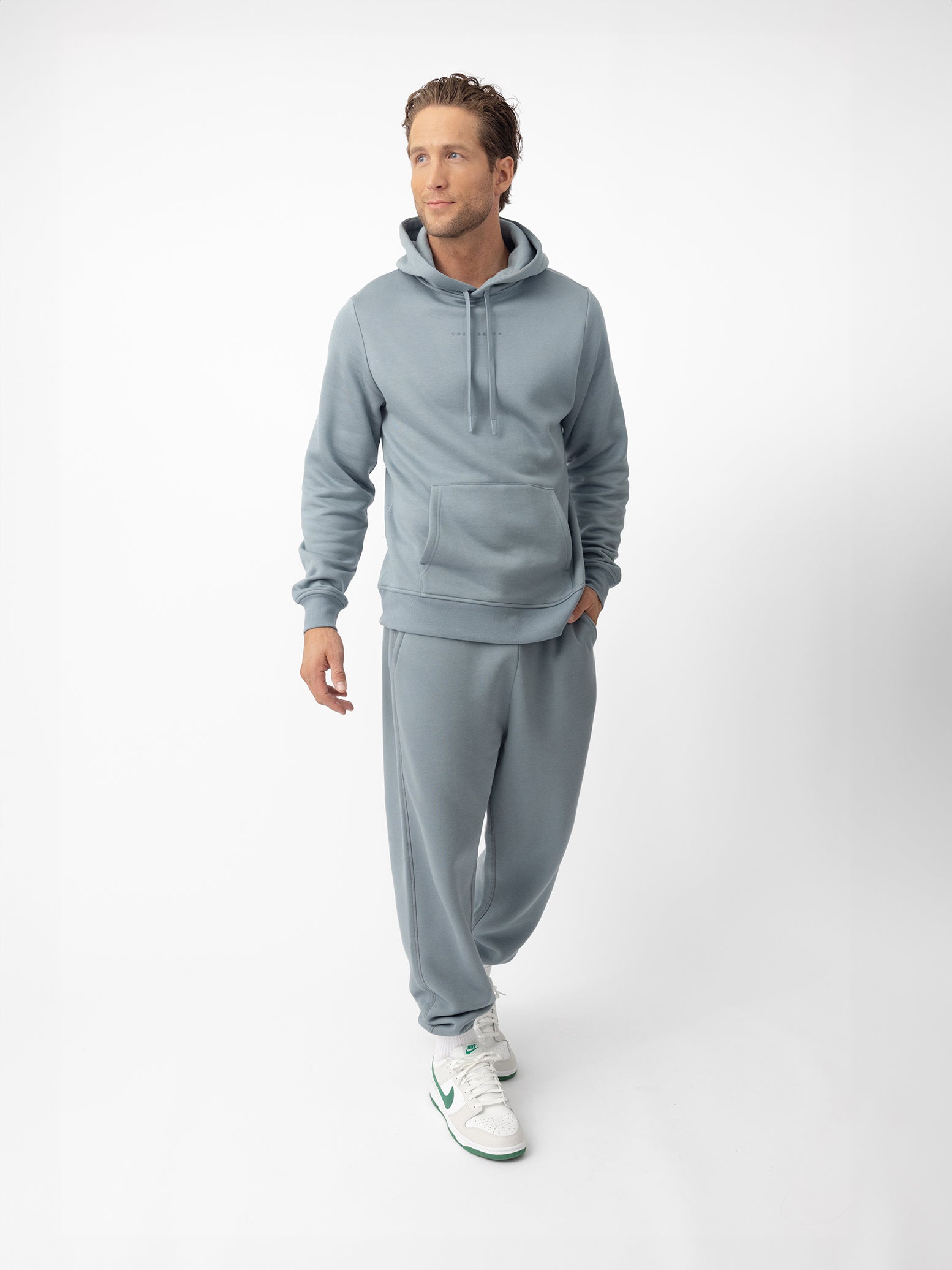 Man wearing smokey blue cityscape hoodie and sweats with white background 