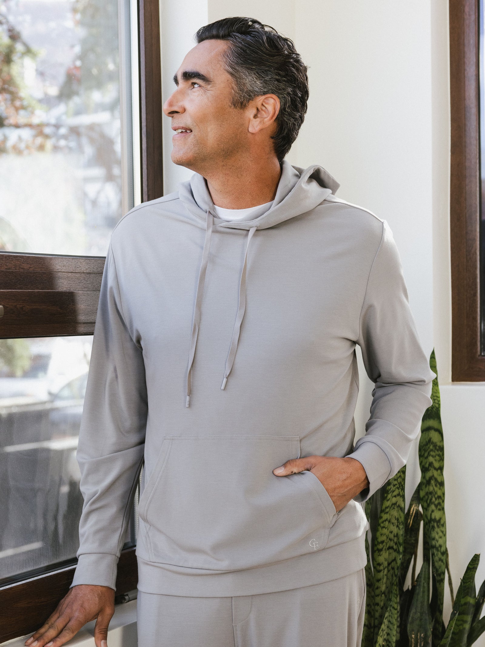 Stone Bamboo Hoodie worn by man standing in front of a window in a house.