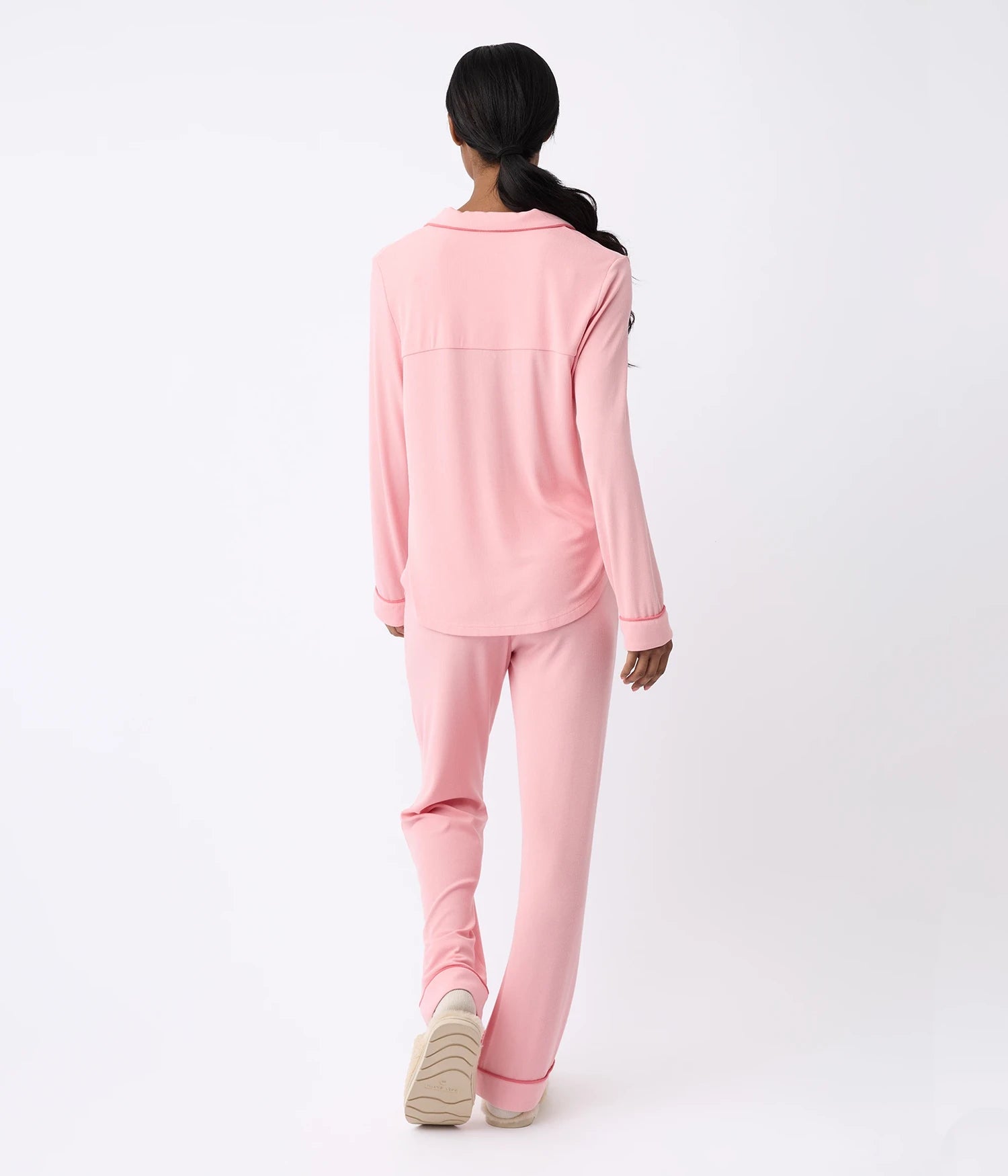 A person with long hair, seen from behind, is wearing the Cozy Earth Rib-Knit Classic Long Sleeve Pajama Set in pink. They are standing on a light background, facing away from the camera.
