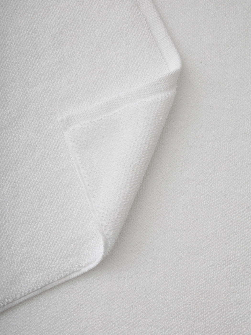 A close-up of the Cozy Earth Loop Terry Bath Mat with a folded corner highlights its soft, textured surface and neatly stitched edges, set against a background of the same material.