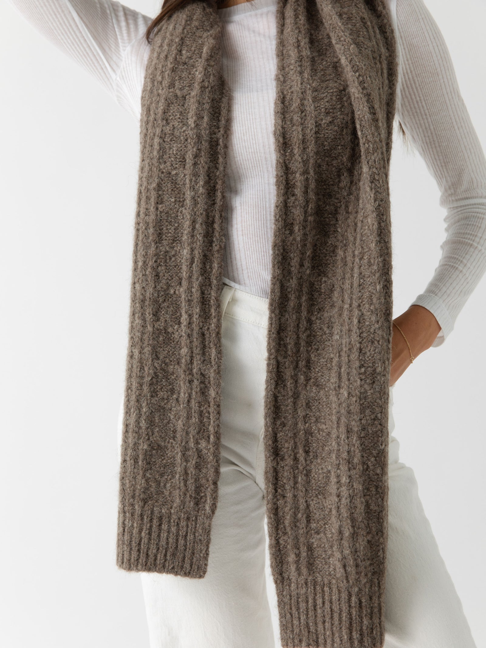 Woman wearing a brown knit cardigan, Cozy Earth Cable Knit Scarf stands in front of a white background
