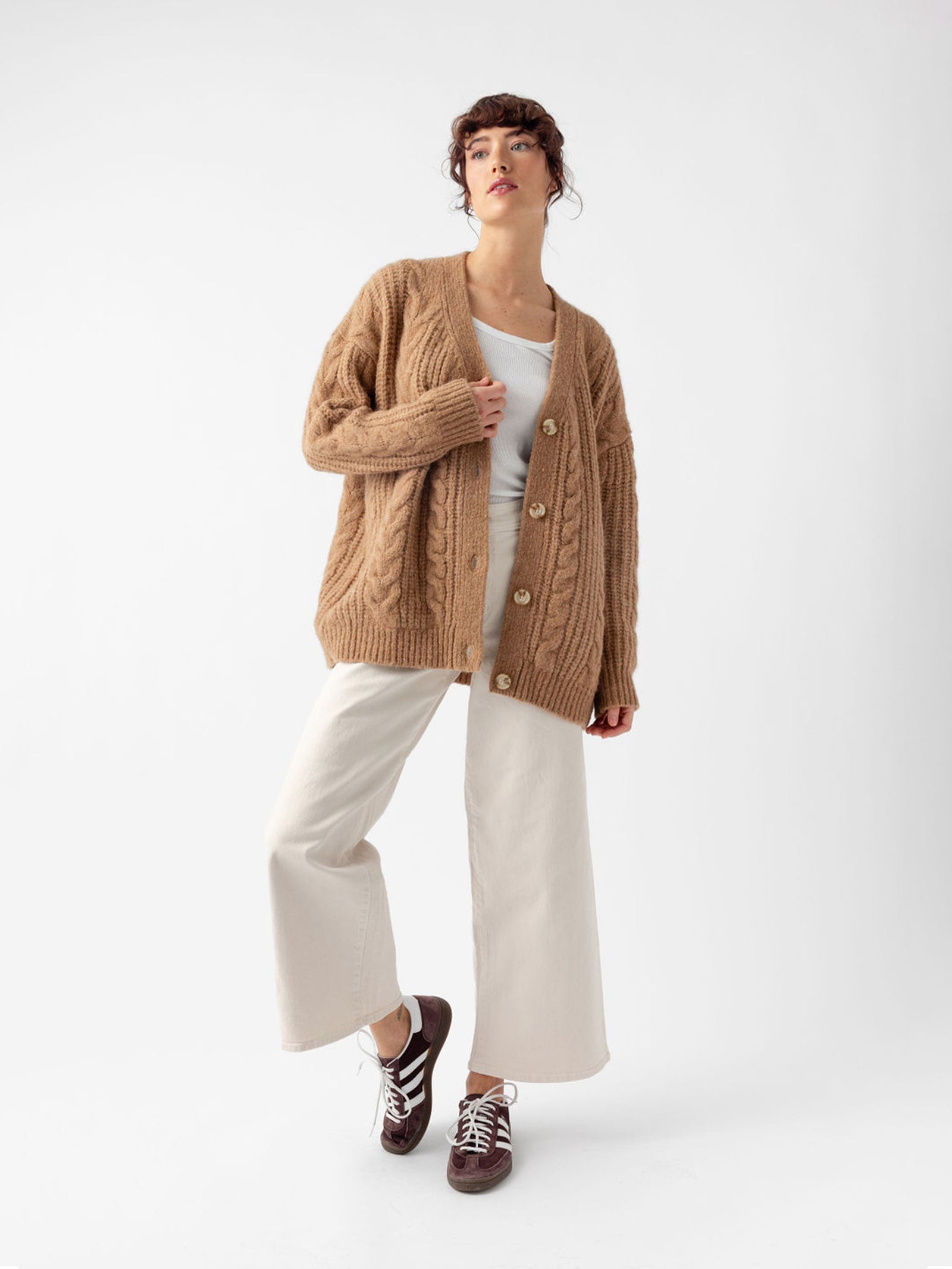 Studio image of woman in camel cardigan and off-white pants