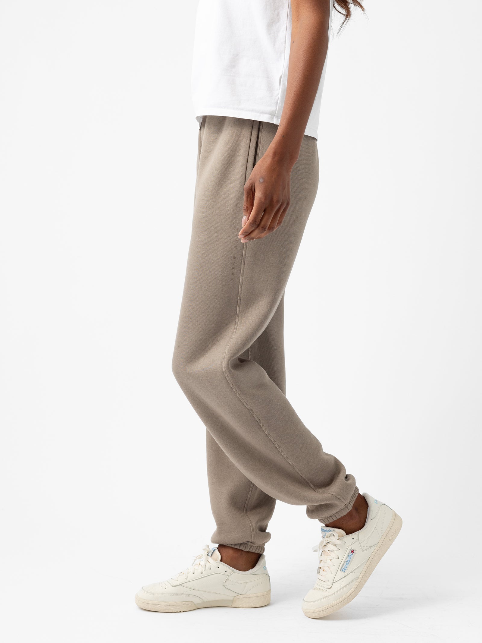 A person wearing the Cozy Earth Women's CityScape Sweatpant in beige and off-white sneakers stands against a plain white background. Their upper body is partially visible, clad in a white top. The sweatpants feature an elastic cuff at the ankles.